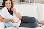 Woman eating popcorn and smiling on the sofa