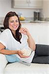 Woman eating popcorn while relaxing on the sofa and smiling