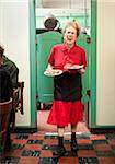 Waitress with curly red hair carrying plates of breakfast and laughing as she walks from the kitchen in a breakfast restaurant in California.