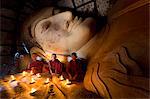 Three novice Buddhist monks sitting by a large reclining Buddha in the light of candles, near Shwesandaw Paya, Bagan, Myanmar (Burma), Asia