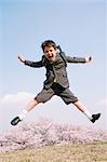 Young boy in school uniform jumping on grassland