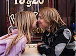 Mother and daughter nose-to-nose on terrace of french cafe, Paris, France