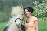 Portrait of a young woman with a icelandic horse standing under a flowering cherry tree in spring, Germany