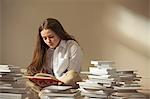 Girl sitting on floor reading surrounded by piles of books