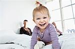 Toddler girl on parent's bed looking at camera, laughing