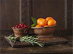 Ingredients to create Clementine and Cranberry Lamb Rack. Clementines in woven wooden bowl, cranberries in small wooden bowl and sprigs of rosemary