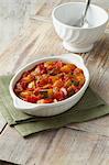 Vegetable ratatouille. Courgettes, tomatoes and red and yellow peppers in white dish on a green cloth