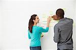 Two colleagues sticking adhesive notes to wall