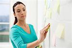 Mid adult woman sticking adhesive notes to wall