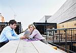 Two people sitting at table using digital tablet outdoors