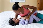 Mother tickling daughter on bed