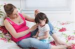 Pregnant woman and toddler daughter on bed looking at smartphone