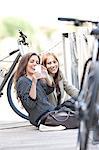 Young women sitting by chain fence photographing themselves