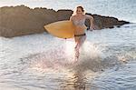 Young woman running in sea with surfboard