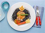 Squid ink noodles,vegetables calamaries and surimi on a plate in the shape of witch's face