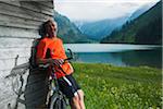 Mature Man leaning against Wooden Building with Mountain Bike, Vilsalpsee, Tannheim Valley, Tyrol, Austria