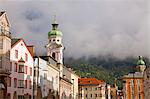 Austria, Tyrol, Innsbruck. One of the church towers and buildings in the historic centre with the alps covered in mist
