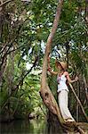 Dominica, Portsmouth. A young woman stands on a tree on the Indian River, one of Dominica's most popular tourist attractions. (MR).