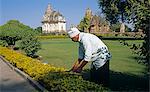 Asia, India, Madhya Pradesh, Khajuraho.  Gardener cutting hedge in early morning light.