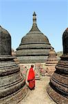 Myanmar, Burma, Rakhine State, Mrauk U. A monk pauses among brick pagodas surrounding the Shittaung Paya, or temple.