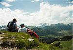 Backview of mature couple sitting on grass, hiking in mountains, Tannheim Valley, Austria
