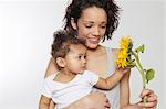 Baby girl touching sunflower held by mother in studio