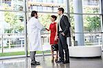 Mature doctor shaking hands with young couple in hospital lobby