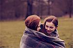 Girls wrapped in a blanket outdoors, smiling