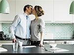 Mid adult woman kissing businessman in kitchen