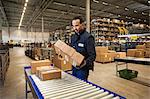 Male warehouse worker selecting cardboard boxes from conveyor belt