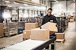 Male warehouse worker checking cardboard box from conveyor belt