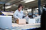 Female warehouse worker packing box for conveyor belt