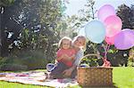 Mother and daughter sitting on blanket in garden with book and balloons