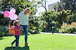 Mother and daughter walking in garden with basket of balloons