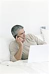 Senior man phoning, in front of a laptop