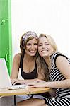 Two young women posing for the camera, laptop
