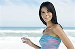 Brown-haired young woman on the beach, holding a glass of water