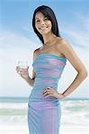 Brown-haired young woman on the beach, holding a glass of water