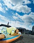 Teenage girl lying on windsurf board on building roof