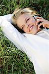 Woman smiling, lying in the grass, on the phone