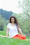 Young woman sitting on a meadow in a flowering cherry tree plantation in spring, Germany