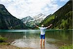 Backview of mature man with arms stretched outward, standing in Lake Vilsalpsee, Tannheim Valley, Austria