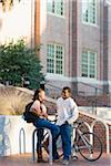 Young man and young woman outdoors on college campus, talking next to bike rack, Florida, USA