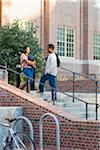 Young man and young woman outdoors on college campus, talking on stairs, Florida, USA