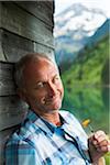 Portrait of mature man looking at camera, holding flower, standing next to building at Lake Vilsalpsee, Tannheim Valley, Austria
