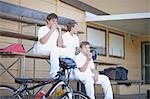 Three boys sitting on bleachers wearing cricket clothes