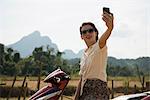 Woman photographing self on moped, Vang Vieng, Laos