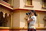 Woman taking photograph outside building, Luang Prabang, Laos