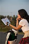 Woman leaning on moped reading book