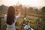 Woman on moped taking photograph in rural scene